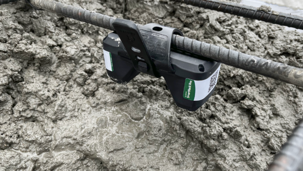 A close-up view of a Giatec SmartRock Pro sensor attached to a rebar chair and embedded in wet concrete for a post tension slab.